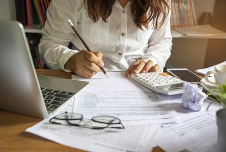 Lady with pencil on paper at desk with laptop and calculator in foreground, getting organised for the Autumn